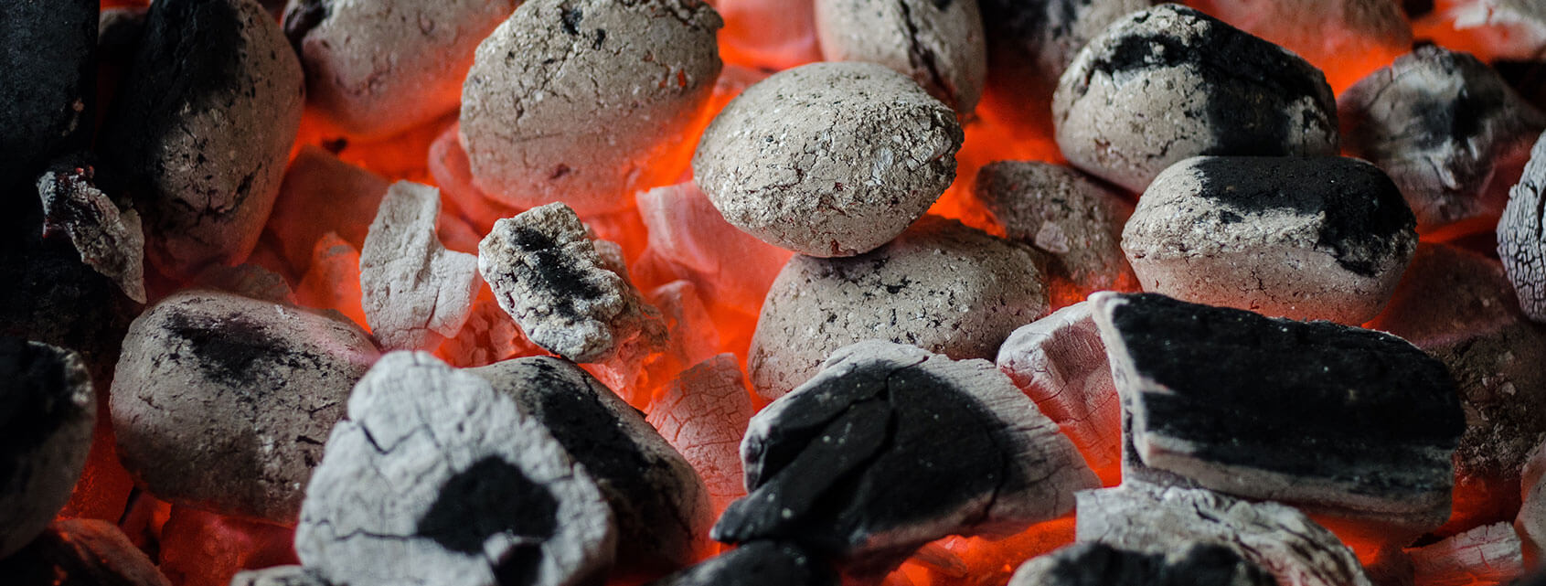 Bird’s-eye view of hot, ashy charcoal briquets with orange flames poking through.