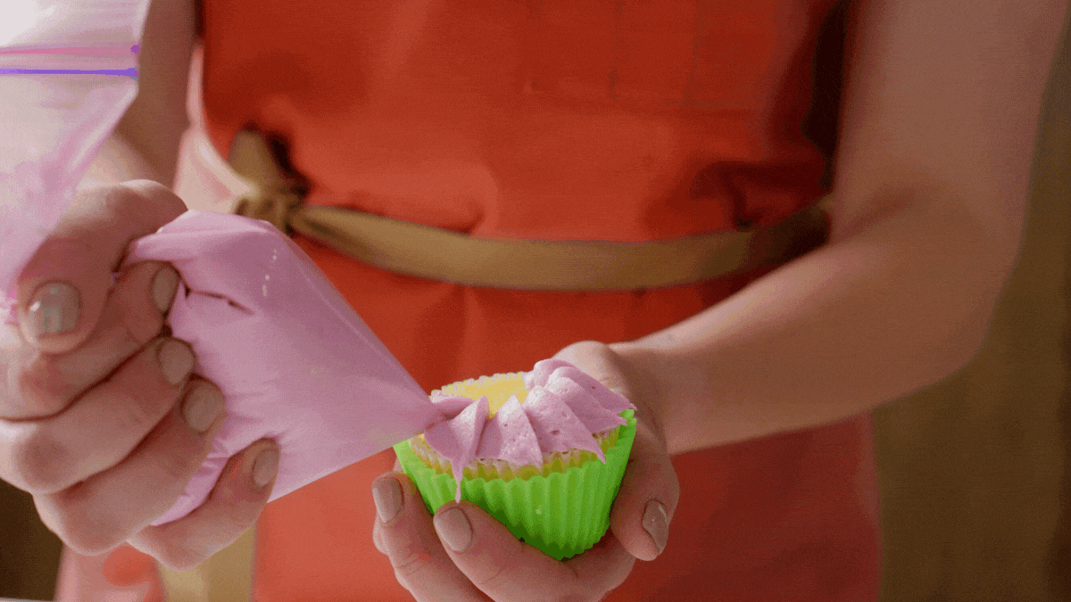 Holding a cupcake while adding petals using frosting in a piping bag with text FLOWER POWER